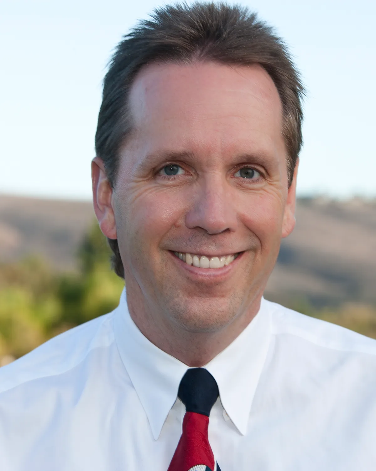 Scott Young, founder and president of ListenToSee, smiling outdoors in a white shirt and tie.